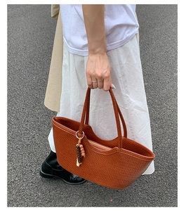 Detail of a brown woven tote bag featuring a decorative wooden beaded pendant charm