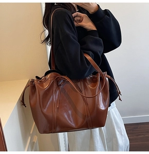 Braune Leder-Tote-Tasche mit Kordelzug-Design, als Schultertasche an einem Modell gezeigt