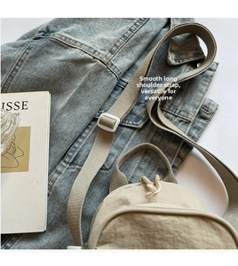 Detail of adjustable strap and zipper on cream canvas crossbody bag over denim cloth