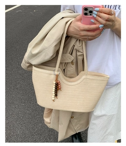 Close-up of cream woven tote bag featuring beaded charm and fine woven texture details