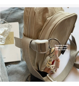Detail of khaki nylon crossbody bag showing durable metal hooks and braided keychain charm