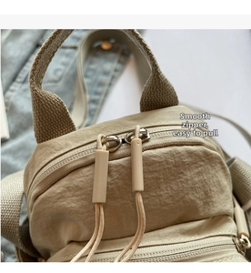 Detailed macro view of the dual-way zipper closure on a beige nylon square crossbody bag