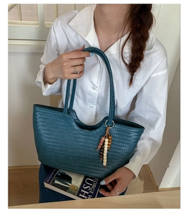 Close-up of dark teal woven tote bag featuring artisan texture and colorful wood bead charm