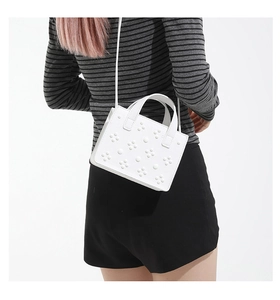 Détail du sac à bandoulière blanc avec motifs floraux texturés sur fond blanc épuré