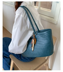 Detail of teal woven tote bag with wooden bead tassel charm on a model's shoulder