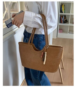 Detailed close-up of a brown woven leather tote bag with a wooden beaded tassel pendant