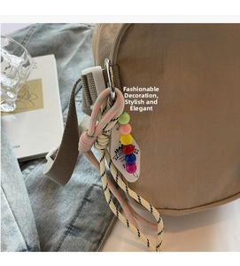 Detail of beige nylon crossbody bag featuring colorful beaded charms and woven cord