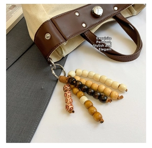 Detalle de colgantes de cuentas de madera y remaches metálicos en bolso de lona