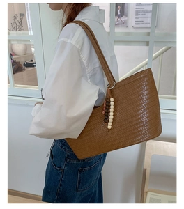 Detailed shot of large brown woven tote bag featuring wooden bead charm on a white shirt