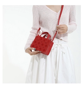 Détail d'un sac bandoulière rouge en cuir à fleurs 3D porté sur un gilet rose doux