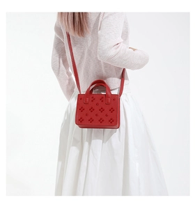 Détail du sac bandoulière rouge en cuir grainé avec rivets floraux 3D sur un modèle
