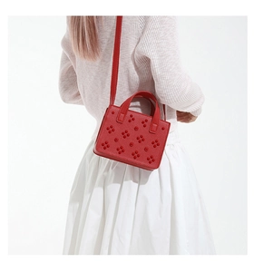Détail du sac rouge en cuir à clous fleuris porté sur une tenue blanche élégante