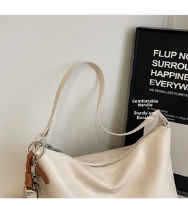Detail of a creamy white dumpling bag with silver zipper and woven bag charm accessory