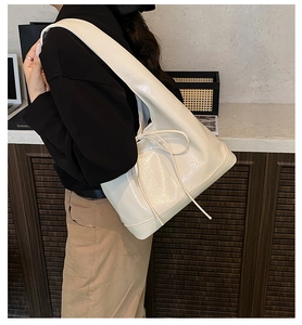 Detail view of cream tote bag with side bow tie and glossy finish on model's shoulder