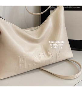 Detail shot of the embossed H.SHAN logo on a soft cream white leather hobo shoulder bag