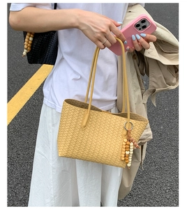 Detail of yellow woven tote bag with wooden bead pendant on model arm for summer style