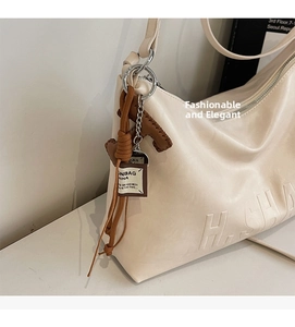 Detail of cream PU leather shoulder bag with side embossing and brown woven charm