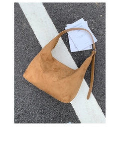 Detail of tan suede crescent tote bag with adjustable strap on urban asphalt background
