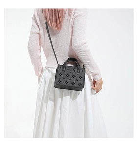 Détail du sac bandoulière carré noir avec rivets floraux 3D et doubles poignées sur mannequin