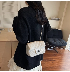 Détail d'un sac bandoulière beige matelassé avec chaîne argentée porté par un mannequin