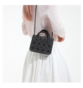 Détail du sac bandoulière en cuir noir avec rivets floraux 3D porté par un mannequin