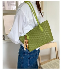 Detail of green woven tote bag with beaded tassel charm on a model in a casual setting