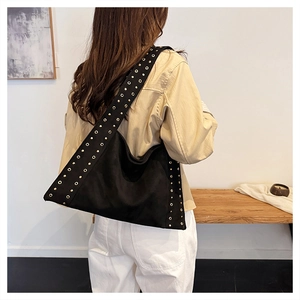 Detail of black suede tote bag featuring metallic gold eyelets and wide shoulder strap
