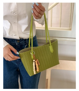 Close-up of green woven tote bag with wooden bead tassel and long shoulder straps