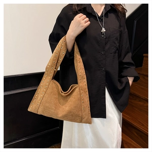 Close-up of brown suede tote bag featuring gold rivet studs on the shoulder strap