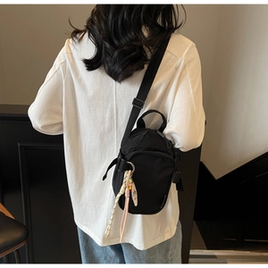 Detail of black nylon mini crossbody bag with multi-zipper layers and woven charm