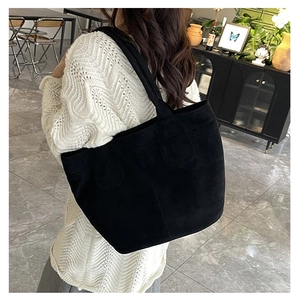 Close-up of a large black matte tote bag worn by a model in a modern indoor setting