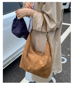 Brown suede hobo bag shown on shoulder with beige trench coat in an outdoor setting