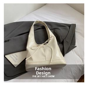 Detail shot of cream glossy faux leather tote bag with a minimalist bow on a grey blazer