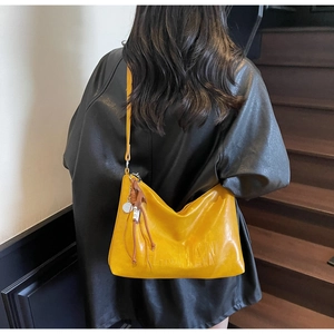 Detail of yellow soft leather hobo bag with embossed lettering and tassel charm on strap