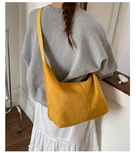 Detail of a ginger yellow suede tote bag worn cross-body by a model in a minimalist setting
