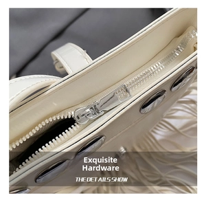 Detail of silver metal zipper and decorative studs on cream leather saddle bag