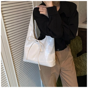 Detail of white glossy leather tote bag with bow detail on a casual indoor outfit