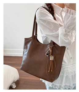 Detail view of deep brown large tote bag with tassel horse charm on a model's shoulder