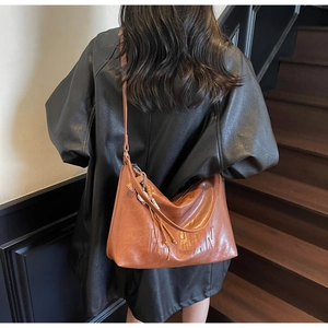 Detailed view of caramel leather shoulder bag with embossed letters and fringe tassel