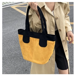 Detail of a large yellow and black tote bag with suede texture and long shoulder straps