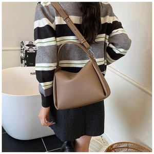 Détail de texture d'un sac hobo en cuir grainé marron porté à l'épaule par un mannequin