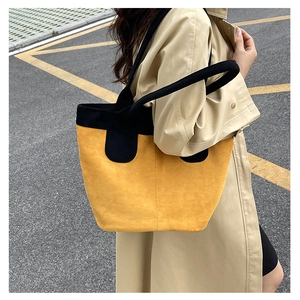 Outdoor shot of a large ginger yellow suede tote bag with black contrast trim handle