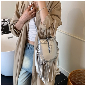 Silver metallic bucket bag with long tassels and rivet details on a magazine background