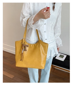 Detail of yellow leather tote bag showing smooth texture and 'T' pendant ornament