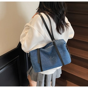 Dettaglio borsa da viaggio in denim blu con manici in pelle nera e fibbia in argento su scala