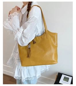 Detail of bright yellow faux leather tote bag with brown ribbon charm and shoulder strap
