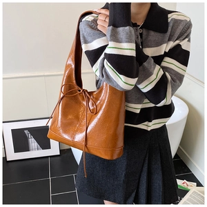 Detail of caramel brown tote bag featuring glossy wrinkled texture and bow decoration