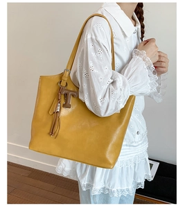 Detail of yellow leather tote bag with T-shaped pendant and tassel for commuting