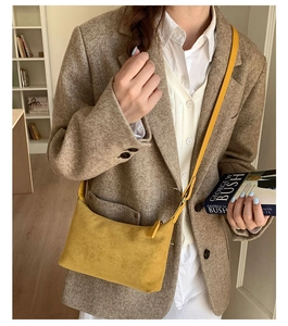 Detail view of yellow suede crossbody bag with long strap and minimalist top zipper design