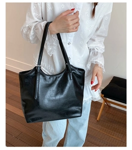 Close-up of black leather tote bag with slender straps and adjustable metal buckle detail